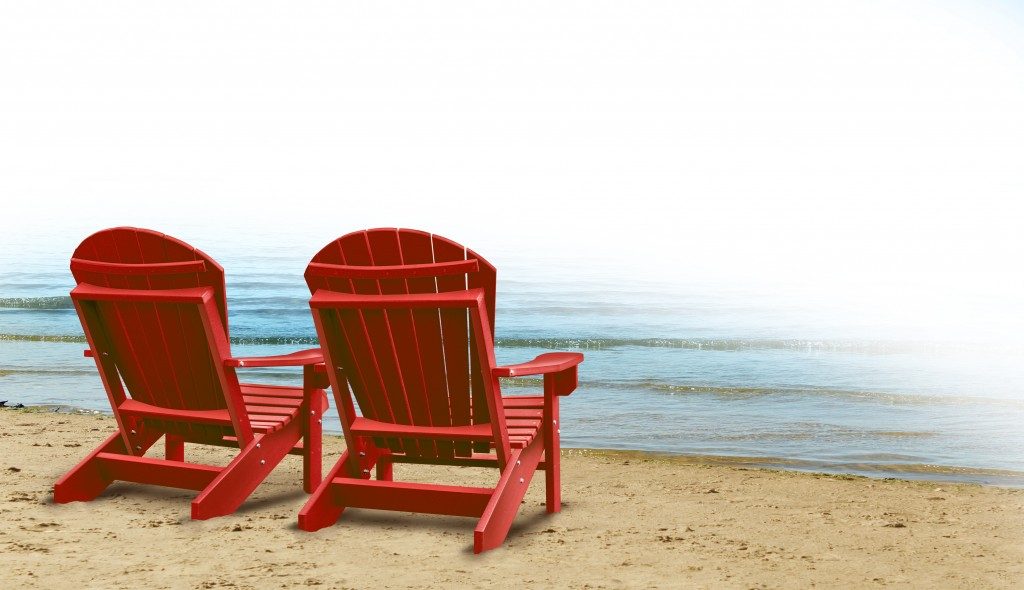 two empty blue adirondack chairs on a tropical sandy beach with ocean view